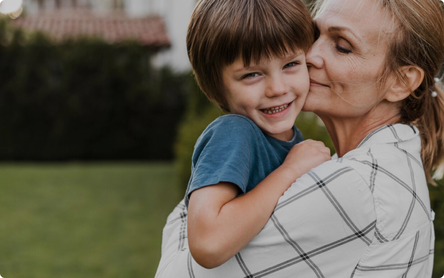 Grandmother hugging a smiling young boy outdoors, conveying family-centred care.