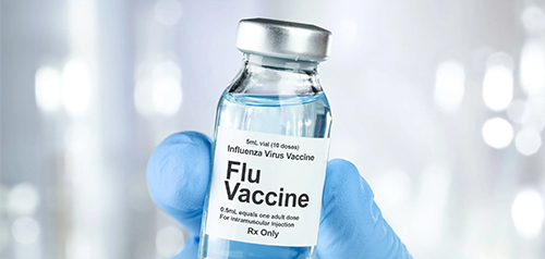 Gloved clinician holding a vial labeled “Flu Vaccine” ready for immunisation at Silverdale Doctors